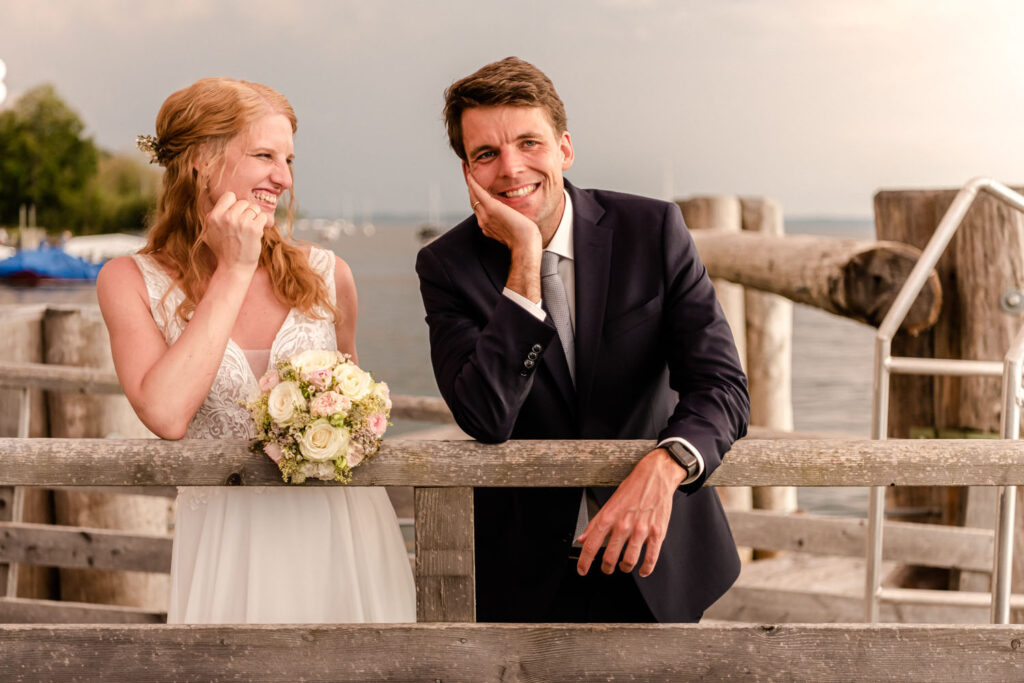 Glücklich lacht die Braut ihren Ehemann an - und das im Abendlicht auf dem Steg am Starnberger See, direkt am Seehotel Leoni.