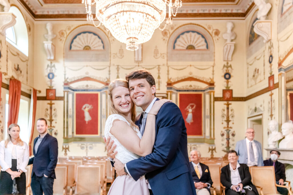 Das verliebte und überglückliche Paar posiert nach der Hochzeit im Standesamt Schloss Ismaning vor der Kamera des Hochzeitsfotografen aus München