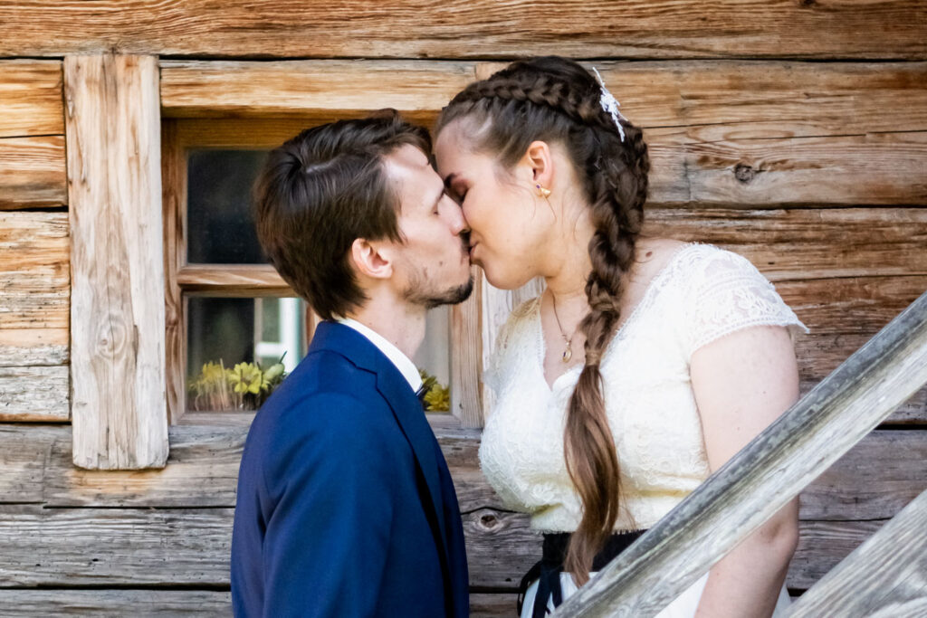 Das Brautpaar küsst sich auf den Stufen des alten Hauses auf der Hochzeit auf der Reiteralm Ainring