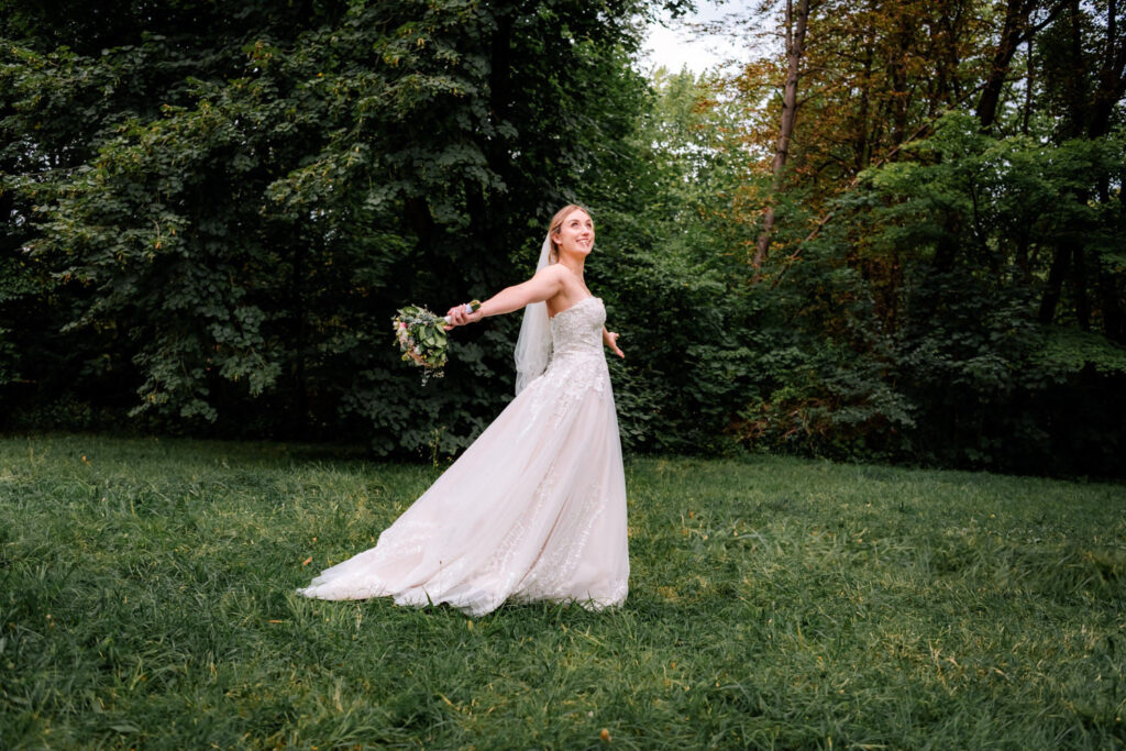 Glücklich tanzt die Braut nach der Hochzeit in der Erlöserkirche in Schwabing durch den Englischen Garten für die Hochzeitsfotografin aus München