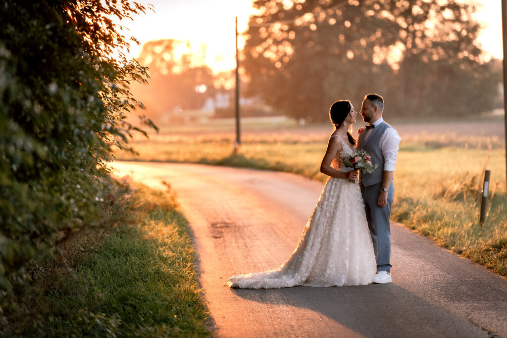 Die Sonne geht gerade unter, die Hochzeitsfotografin spaziert mit dem Brautpaar nach der Hochzeit durch die Landschaft rund um die Alte Tenne Eder am Holz. So entstehen die schönsten Bilder!