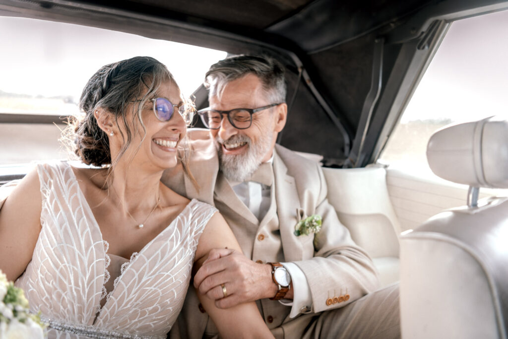 Nach der Hochzeit in Landsberg am Lech fährt das Paar mit den Oldtimer zur großen Feier und strahlt verliebt für die Kamera der Hochzeitsfsotografin aus München