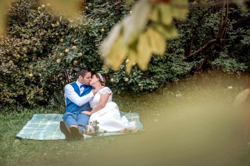 Entspannt sitzt das Brautpaar bei Fotoshooting auf einer Decke im Park, bevor es zur Feier der Hochzeit in den Lindenkeller in Freising geht