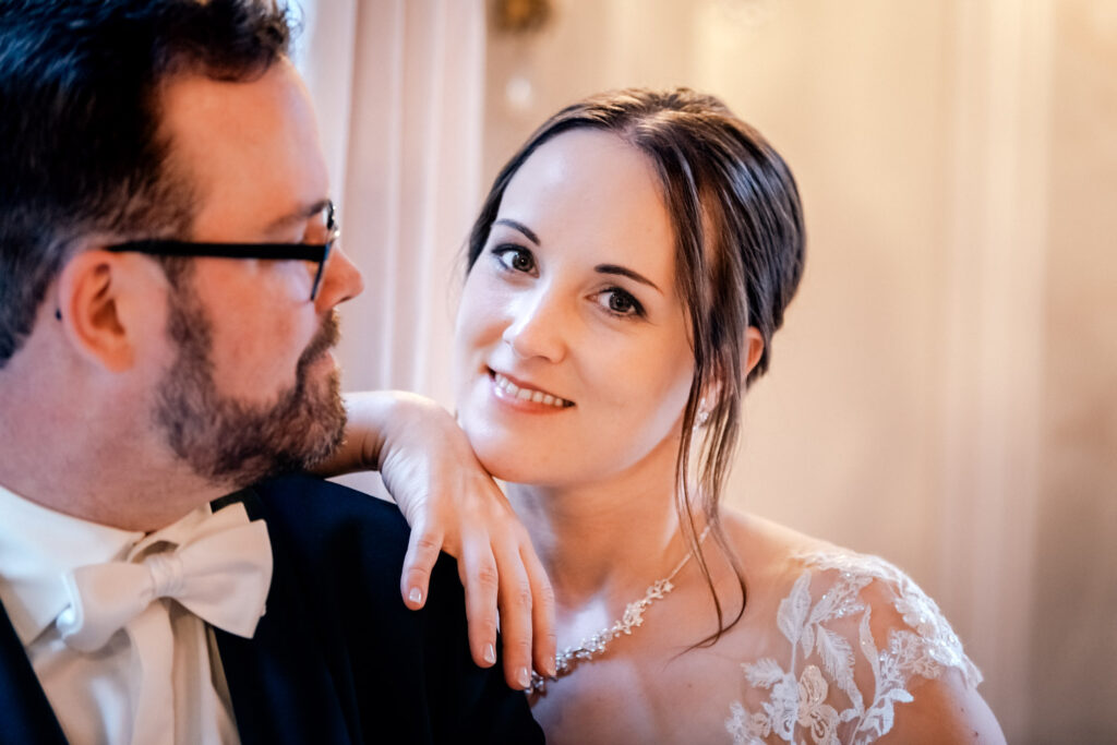 Die Braut lächelt in die Kamera der Hochzeitsfototgrafin während sie sich an ihren Schatz anschmiegt.